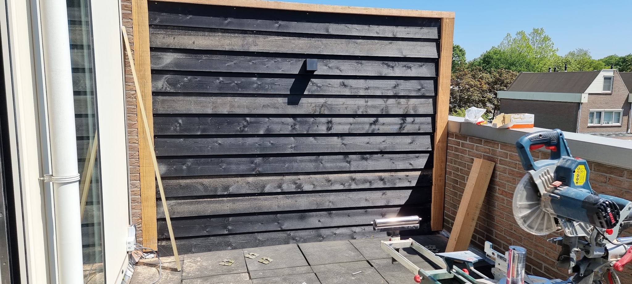 Zwarte houten schutting in aanbouw, met afkortzaag op de klus