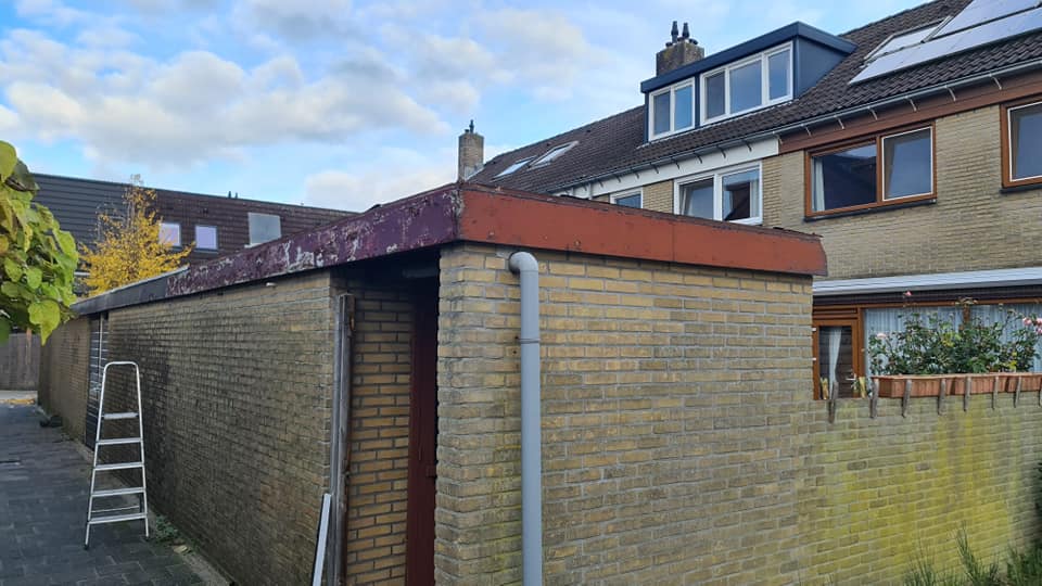 Gemetselde schuur achter rijtjeshuizen, ladder tegen de muur