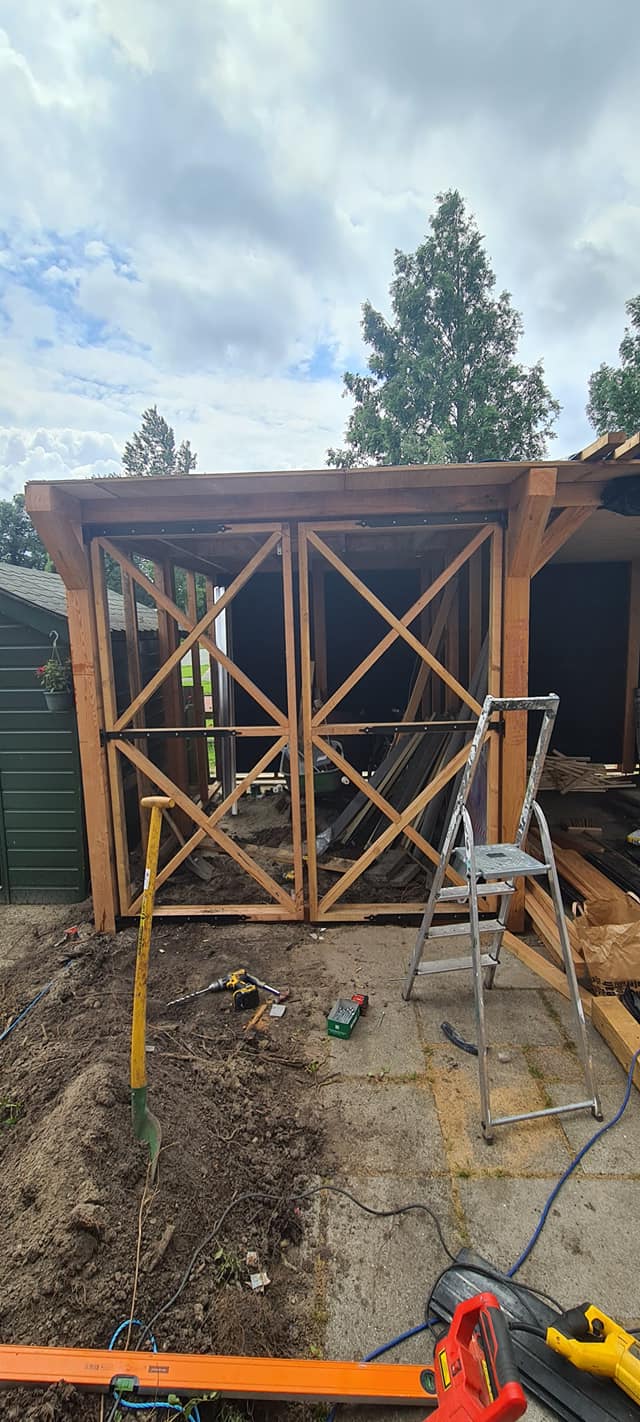 Houten overkapping in aanbouw in een tuin, met ladder en gereedschap